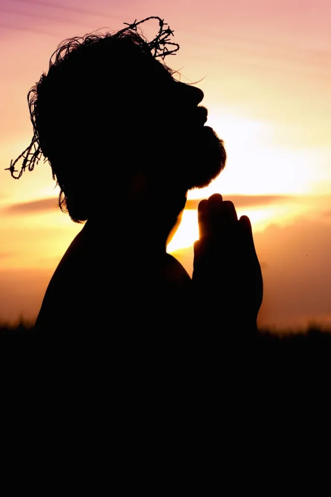 Silueta de una persona rezando con las manos juntas al atardecer